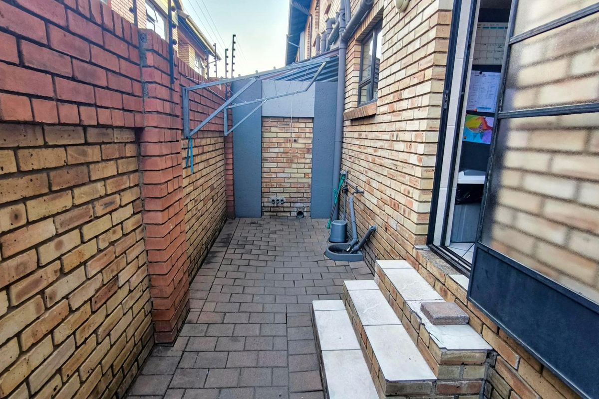 A paved rear courtyard area featuring brick boundary walls, external plumbing connections, and tiled steps leading to the interior of the townhouse.