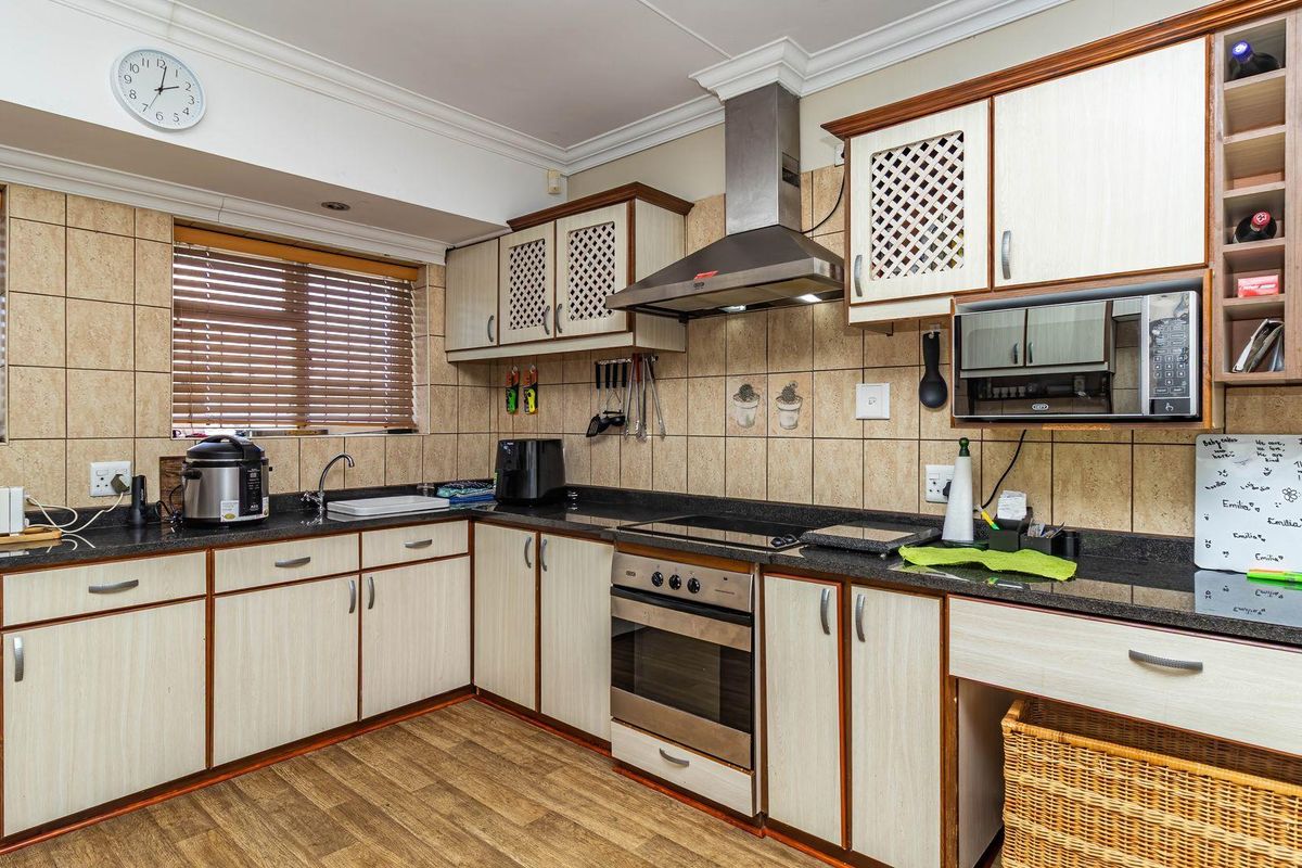 A functional kitchen featuring granite countertops, built-in oven, extractor fan, and ample cabinetry with a tiled splashback and wood-look flooring.