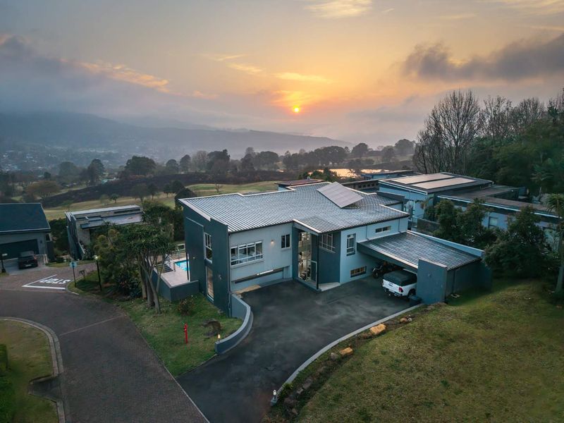 Aerial view of a modern multi-level residence featuring a metal roof with solar panels, a paved driveway, carport, and a swimming pool at sunset.