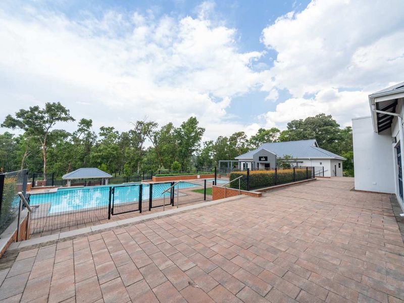 A well-maintained outdoor pool area featuring paved terrace space, secure metal fencing, and a gazebo, set within a landscaped estate environment.