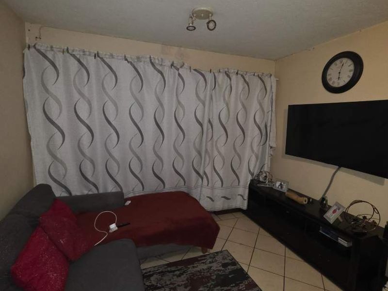 A living room featuring tiled flooring and a ceiling light fixture, showing signs of water damage on the wall.