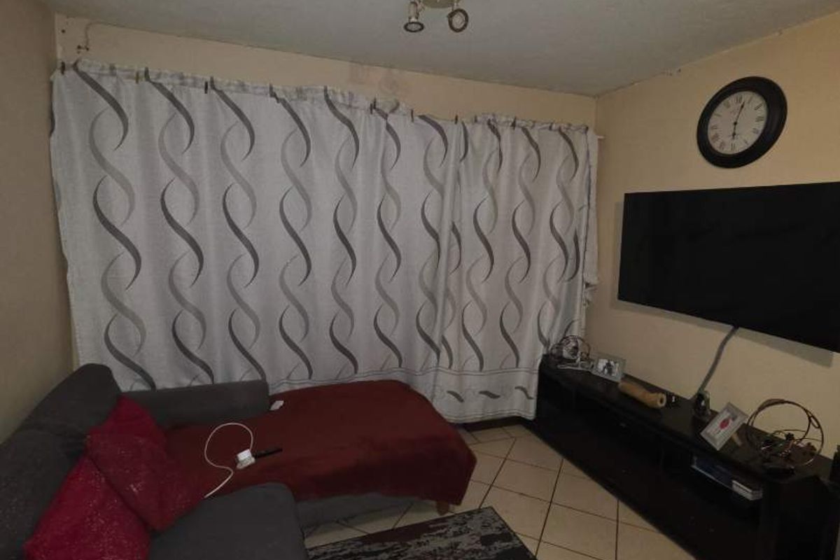 A living room featuring tiled flooring and a ceiling light fixture, showing signs of water damage on the wall.