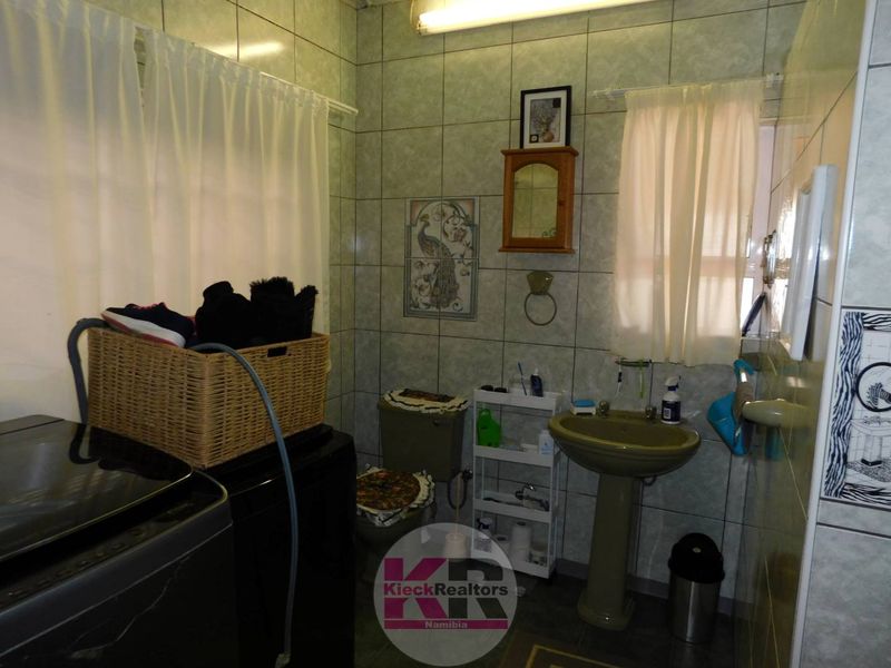 A functional bathroom featuring a pedestal sink, toilet, and full-height ceramic wall tiling.