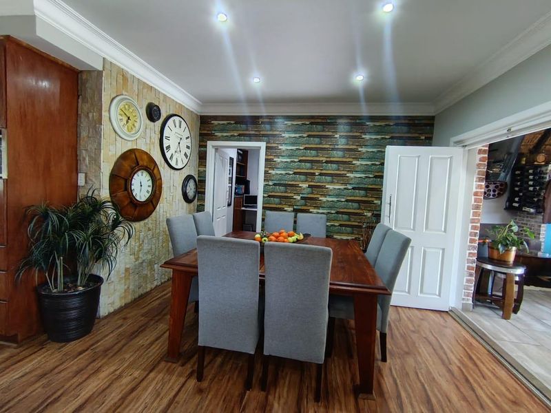 Dining room featuring timber laminate flooring, recessed downlights, and a decorative stone-clad feature wall with access to an adjacent room.