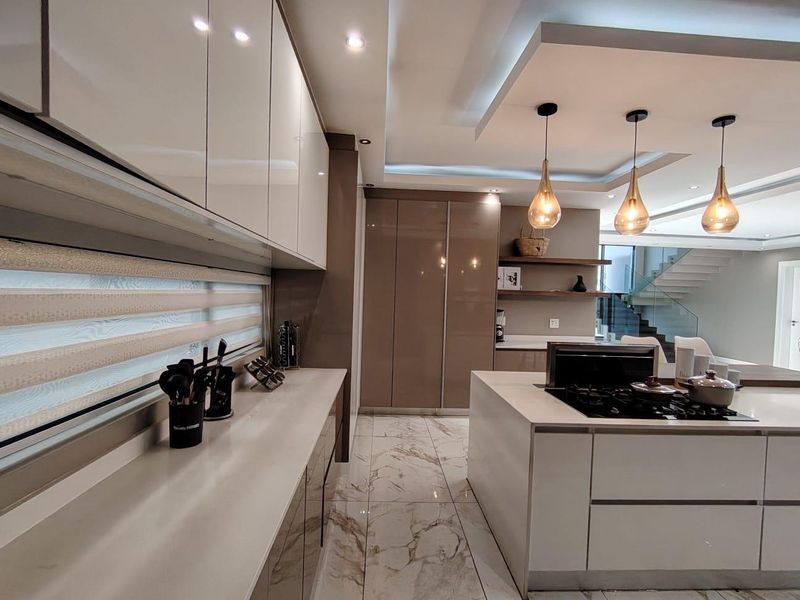 Modern kitchen featuring high-gloss cabinetry, a central island with a gas cooktop, stone countertops, and elegant pendant lighting with marble-look flooring.