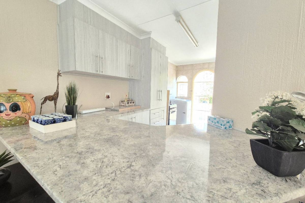 A functional kitchen area featuring light-toned cabinetry, stone-look countertops, and a breakfast bar, with an adjacent utility space visible in the background.