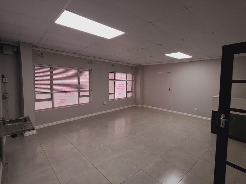 A vacant office space featuring tiled flooring, a drop ceiling with recessed lighting, and a built-in stainless steel sink unit.