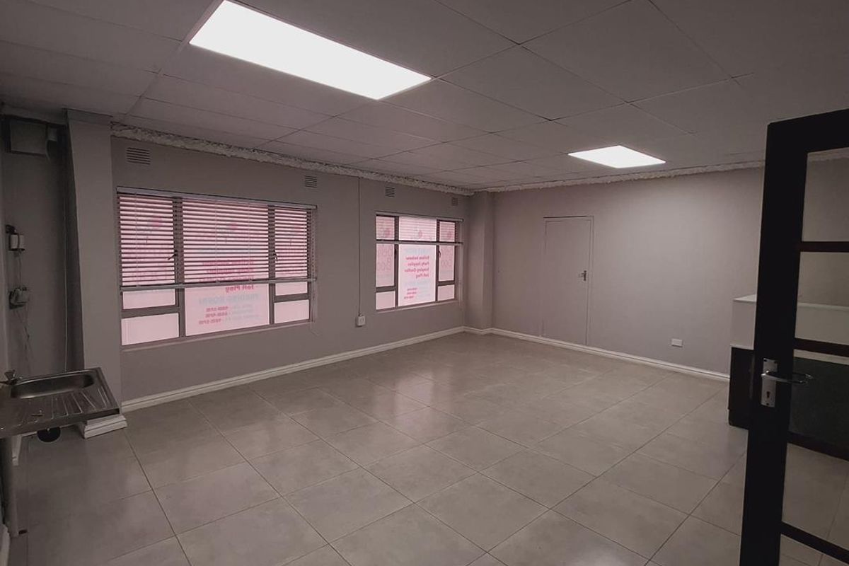 A vacant office space featuring tiled flooring, a drop ceiling with recessed lighting, and a built-in stainless steel sink unit.