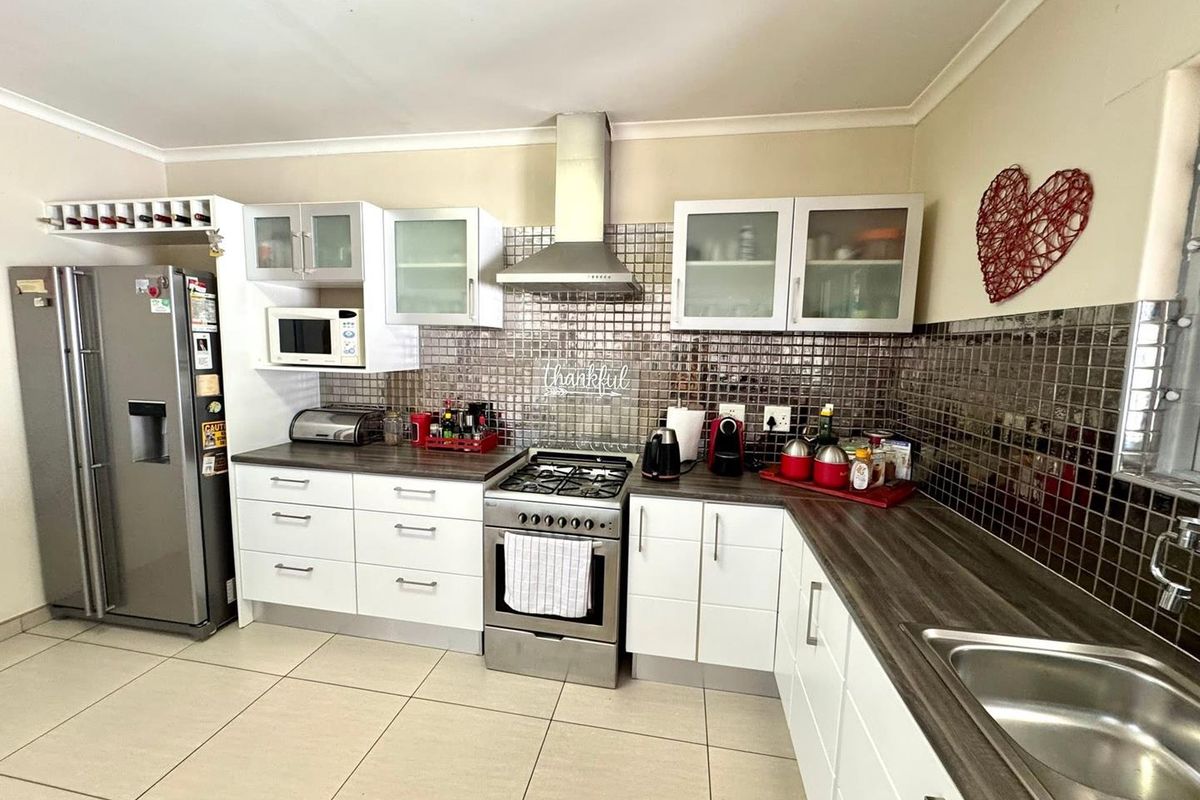 A functional kitchen featuring white cabinetry, dark laminate countertops, a gas stove with extractor fan, and a modern tiled backsplash.