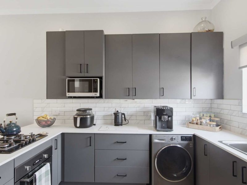 Modern kitchen featuring dark grey cabinetry, white stone countertops, subway tile backsplash, integrated appliances, and a built-in gas cooktop with oven.