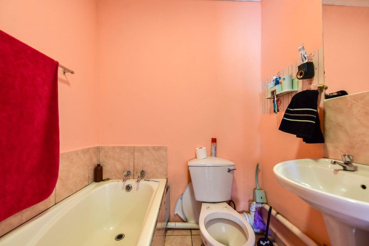 A functional bathroom featuring a bathtub, pedestal basin, and toilet, with tiled splashbacks and flooring. The space would benefit from cosmetic updates.