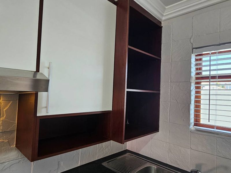 A compact kitchen area featuring built-in cabinetry, a stainless steel extractor fan, and a sink, finished with textured wall tiles.