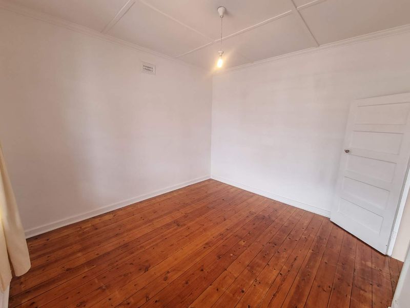 A vacant bedroom featuring polished timber floorboards, a classic panelled ceiling, and neutral white walls, offering a clean canvas for personalization.