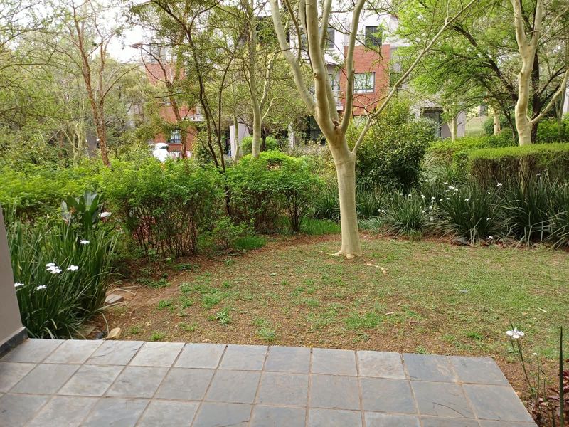 A private garden area featuring a tiled patio and established trees, providing a peaceful outdoor space for the apartment.