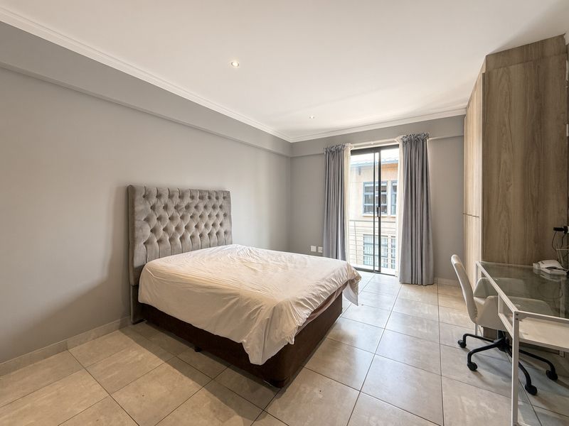 A well-maintained bedroom featuring neutral tiled flooring, built-in wooden cupboards, and a sliding glass door providing access to a balcony.