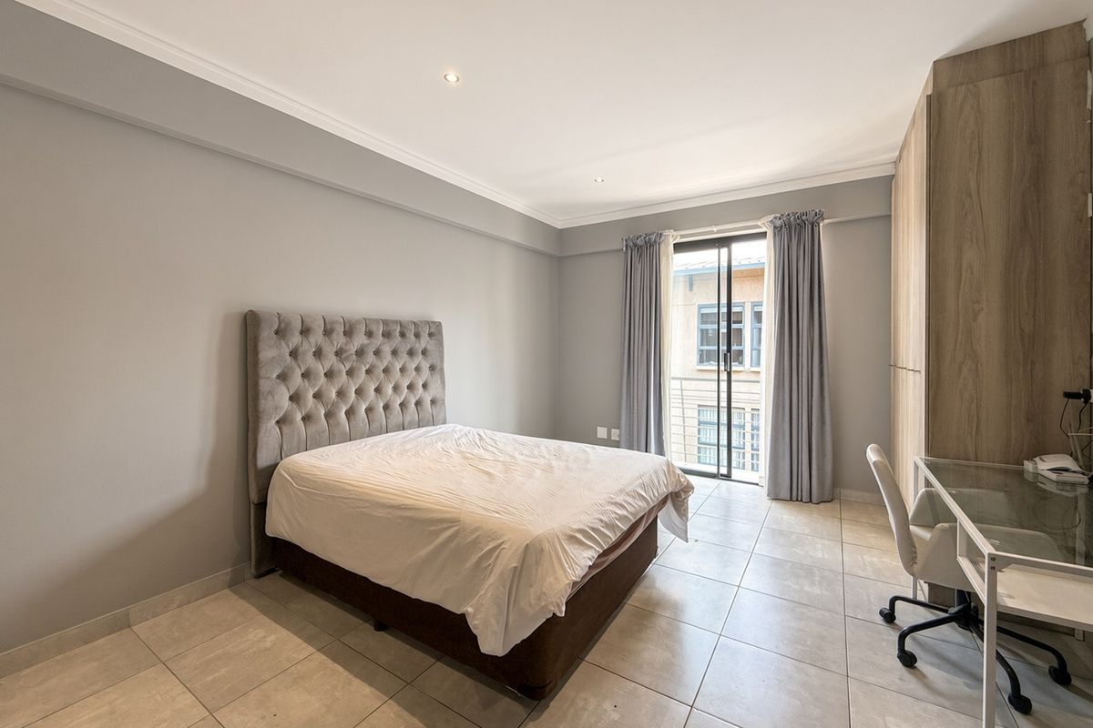 A well-maintained bedroom featuring neutral tiled flooring, built-in wooden cupboards, and a sliding glass door providing access to a balcony.