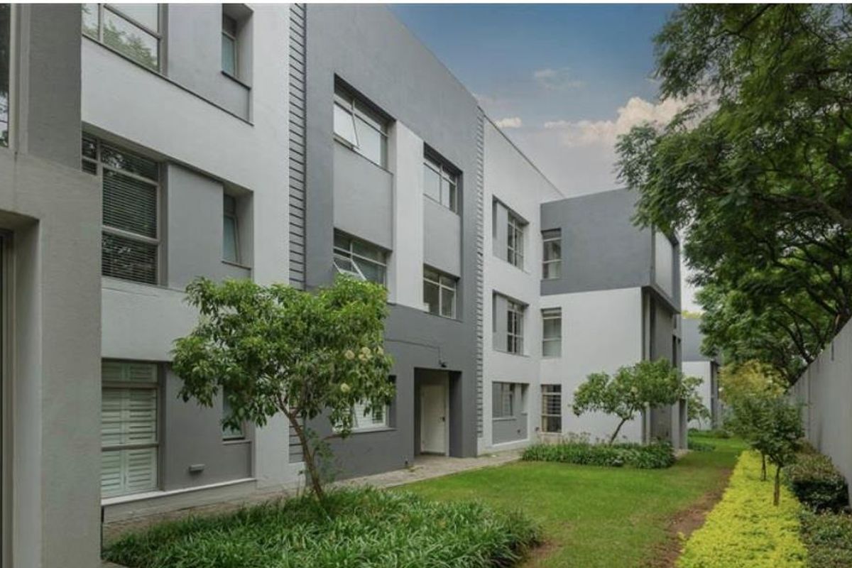 A view of the apartment complex rear facade featuring modern grey and white exterior finishes, landscaped garden areas, and established trees.