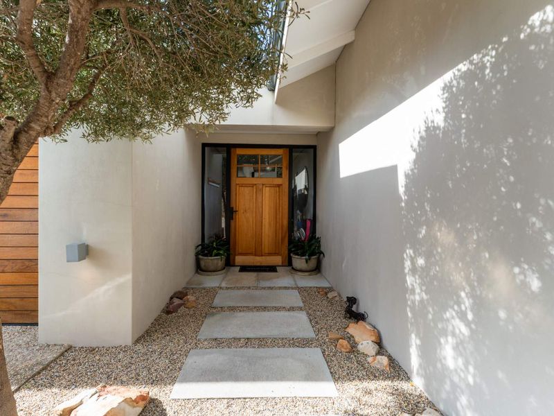 A welcoming front entrance featuring a solid timber door, concrete paver pathway, and gravel landscaping, framed by modern exterior walls.