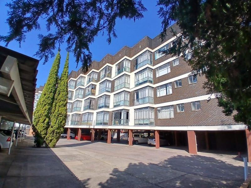 Exterior view of a multi-story apartment building featuring brick facade, enclosed balconies, and a ground-level covered parking area.