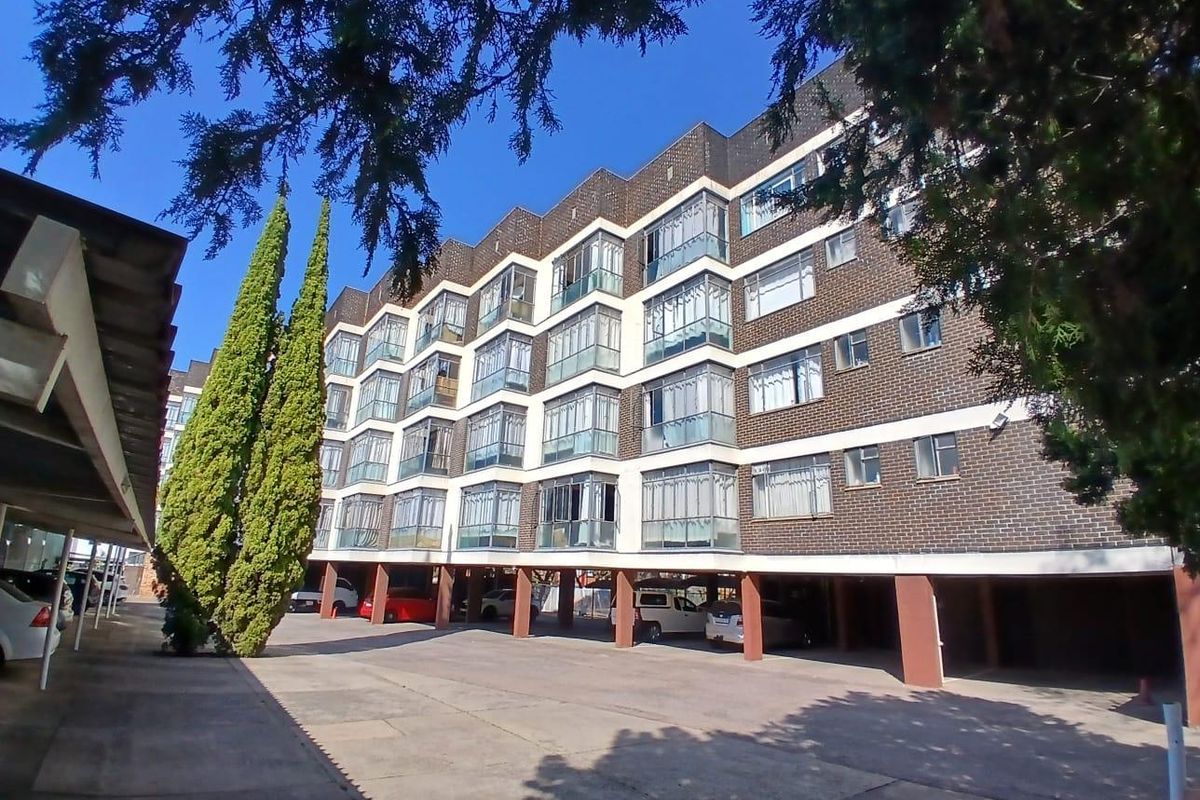 Exterior view of a multi-story apartment building featuring brick facade, enclosed balconies, and a ground-level covered parking area.