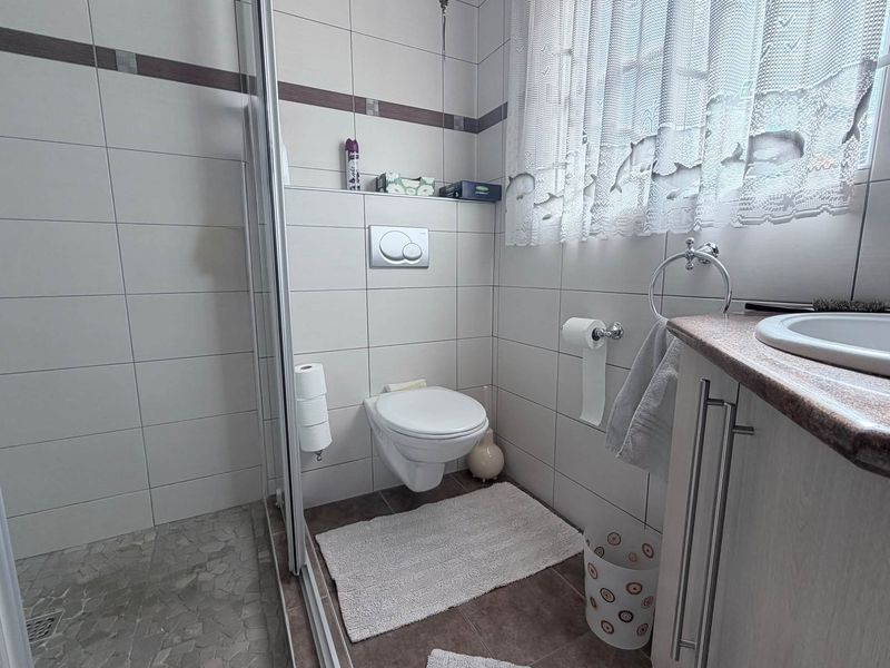A functional bathroom featuring a wall-mounted toilet, a glass-enclosed shower, and a vanity unit with an integrated sink.