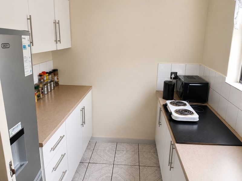 A compact kitchen featuring white cabinetry, laminate countertops, tiled backsplash, and tiled flooring, providing a functional and clean workspace.