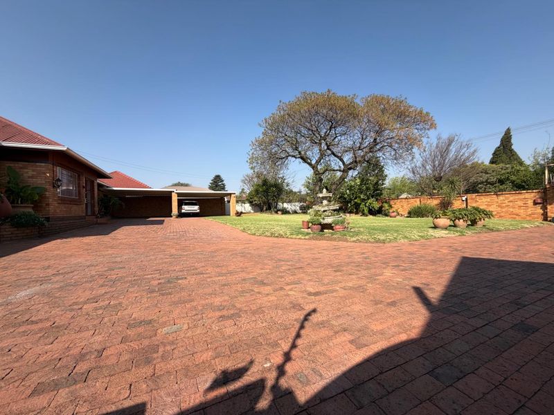 Spacious front exterior featuring extensive brick paving, a large carport, and a well-maintained garden area with a brick boundary wall.