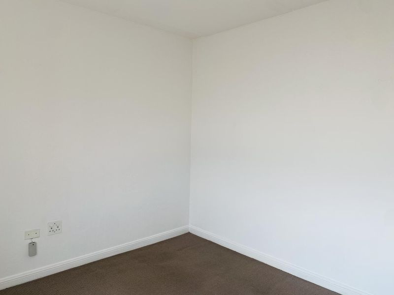A clean, empty bedroom corner featuring neutral wall paint, carpeted flooring, and standard electrical power outlets.