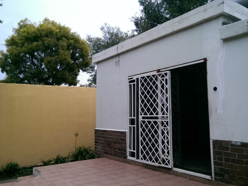 Rear exterior view of the office building featuring a tiled patio, sliding door with security gate, and a surrounding boundary wall.