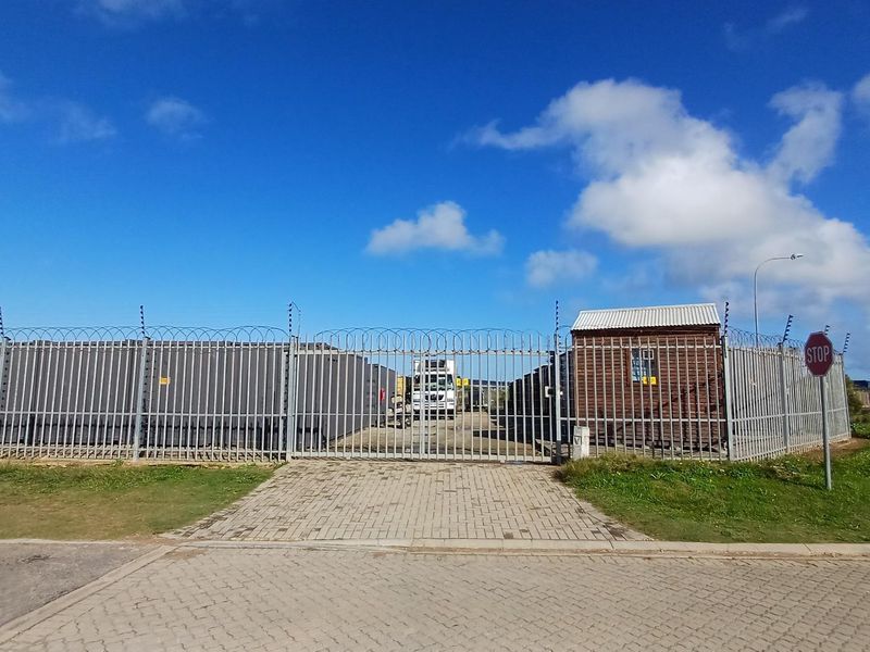 Industrial property entrance featuring a secure gated access point with perimeter fencing, razor wire, and a small guard hut.