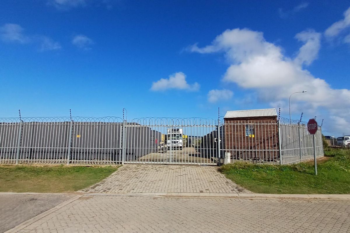 Industrial property entrance featuring a secure gated access point with perimeter fencing, razor wire, and a small guard hut.