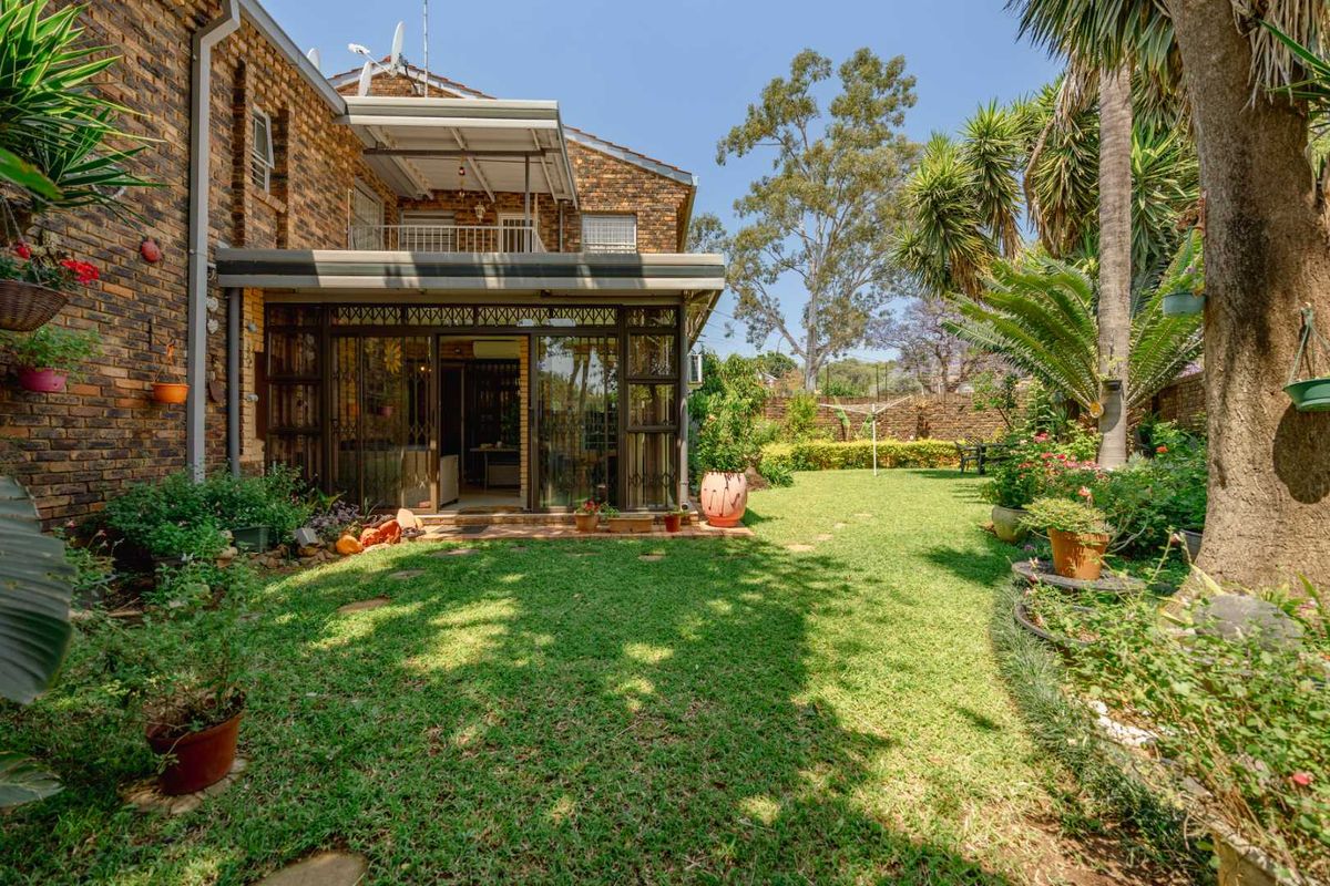 Rear view of a face brick townhouse featuring a covered patio, upper balcony, and a well-maintained private garden.