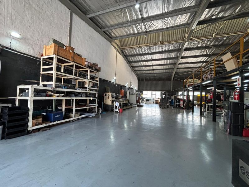 Spacious industrial warehouse featuring high ceilings with exposed steel trusses, durable epoxy flooring, and a functional mezzanine level for additional storage or workspace.