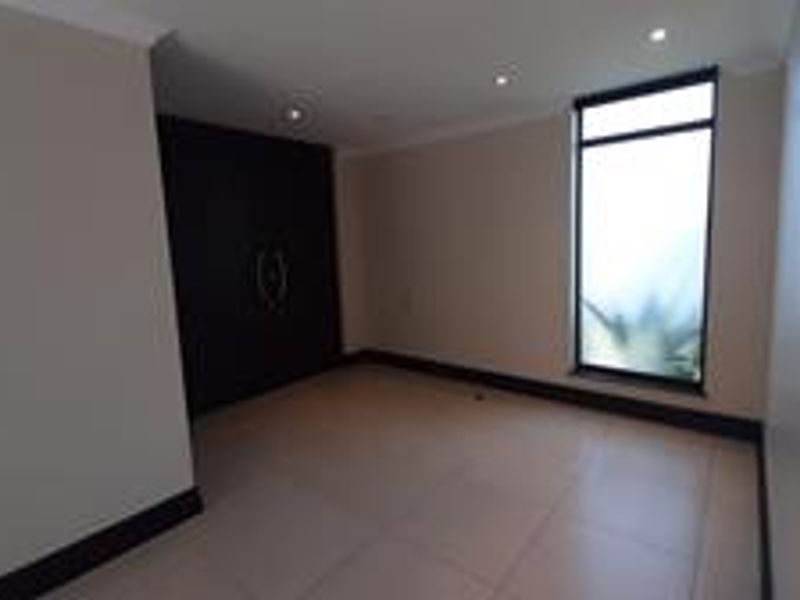A spacious, empty bedroom featuring neutral tiled flooring, recessed downlighting, and dark built-in cupboards, offering a clean and modern blank canvas.