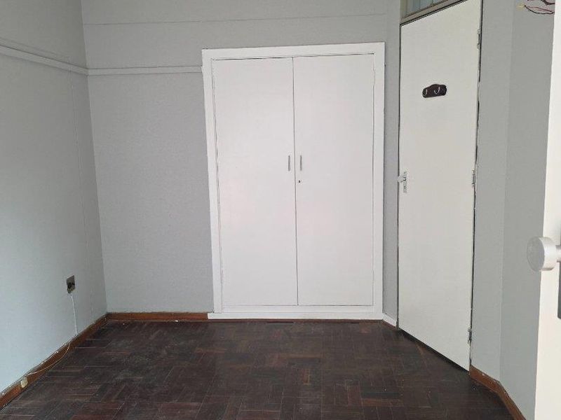 An empty bedroom featuring original parquet flooring, a built-in wardrobe, and a neutral wall finish, offering a blank canvas for personalization.