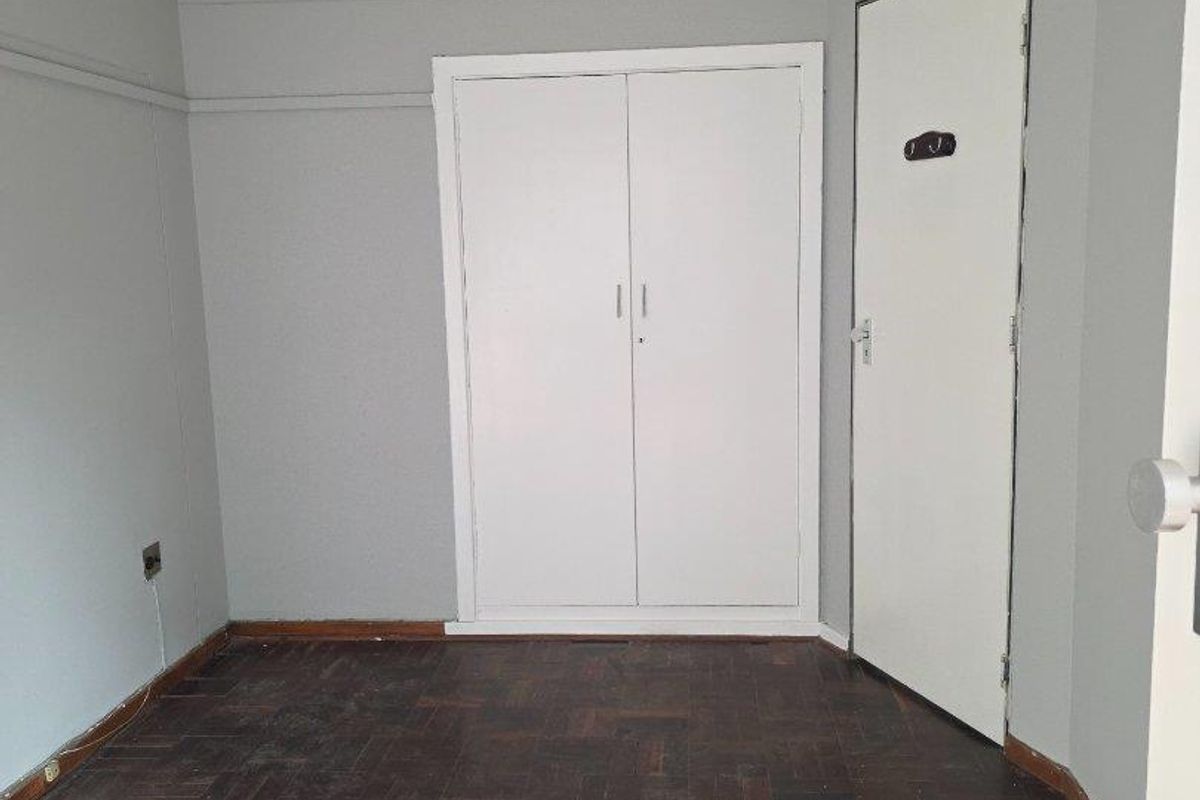 An empty bedroom featuring original parquet flooring, a built-in wardrobe, and a neutral wall finish, offering a blank canvas for personalization.