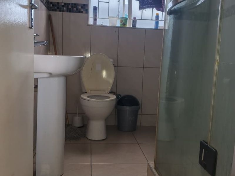 A functional bathroom featuring a pedestal basin, toilet, and a glass-enclosed shower with tiled finishes throughout.