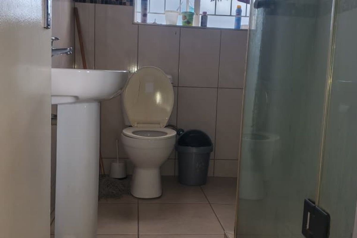 A functional bathroom featuring a pedestal basin, toilet, and a glass-enclosed shower with tiled finishes throughout.