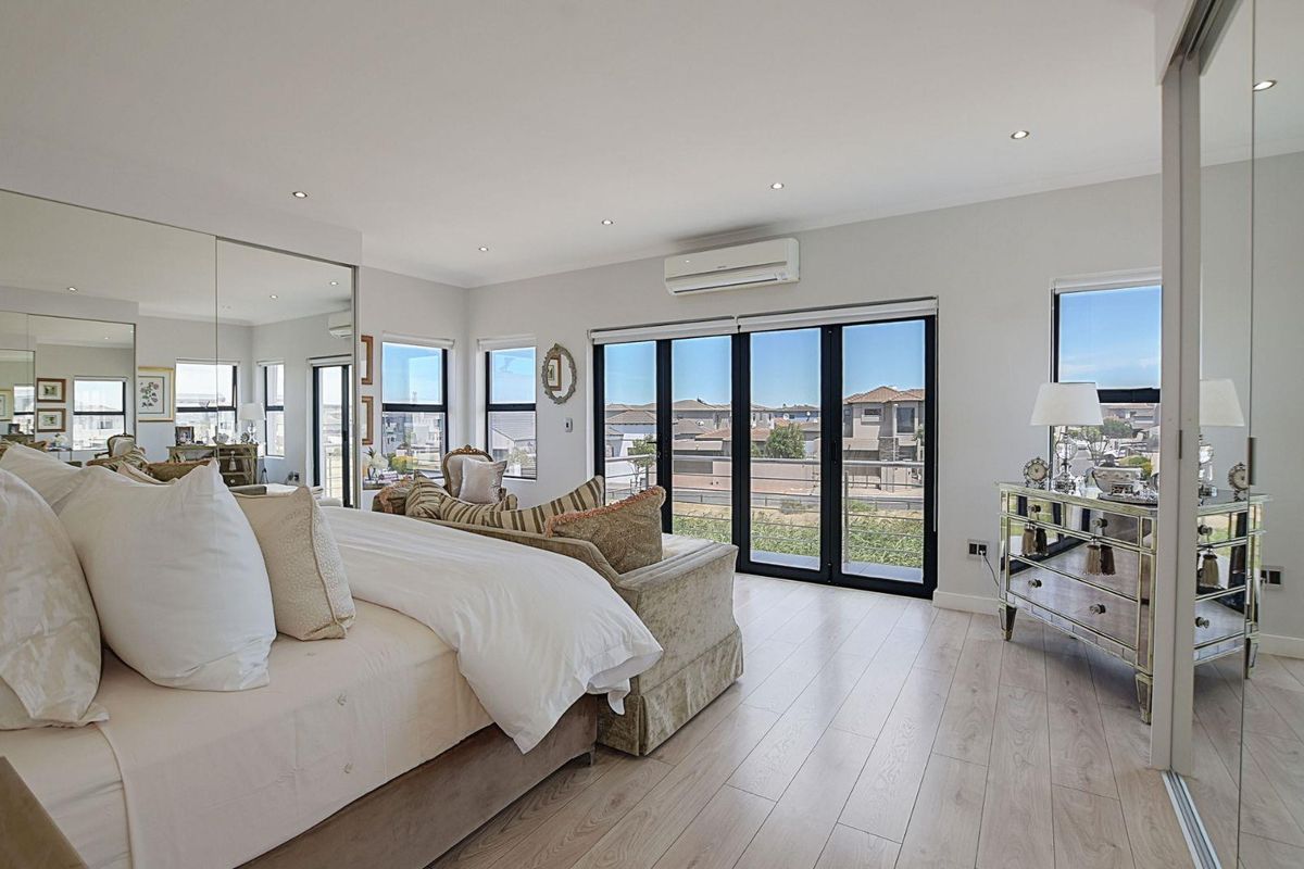 Spacious bedroom featuring light wood-look flooring, recessed downlighting, a wall-mounted air conditioning unit, and large black-framed sliding doors opening to a balcony.