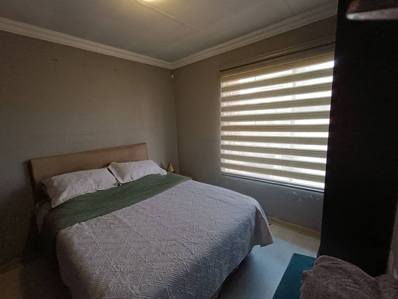 A functional bedroom featuring neutral wall tones, laminate flooring, and modern roller blinds, providing a comfortable and well-lit sleeping space.