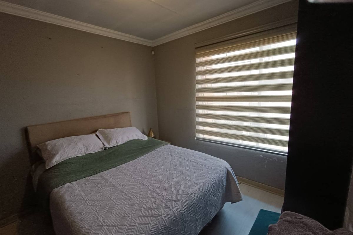 A functional bedroom featuring neutral wall tones, laminate flooring, and modern roller blinds, providing a comfortable and well-lit sleeping space.