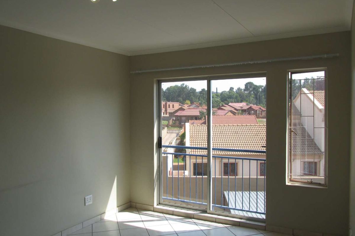 An empty living room featuring tiled flooring, a sliding glass door leading to a balcony, and security bars on the windows.