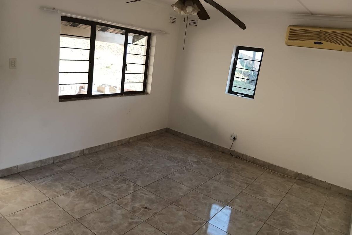 An empty bedroom featuring tiled flooring, a ceiling fan, and a wall-mounted air conditioning unit with security bars on the windows.