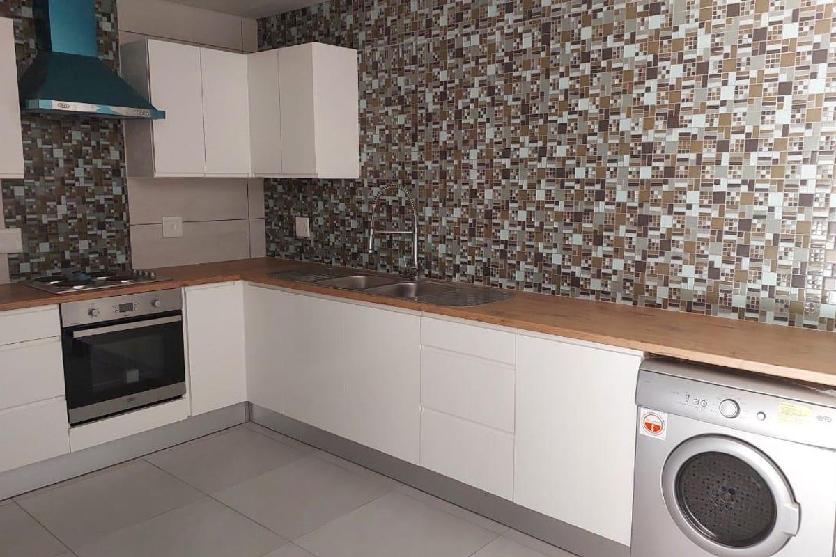 Modern kitchen featuring white cabinetry, wood-look countertops, mosaic tile backsplash, built-in oven, gas hob, extractor fan, and integrated laundry appliance space.