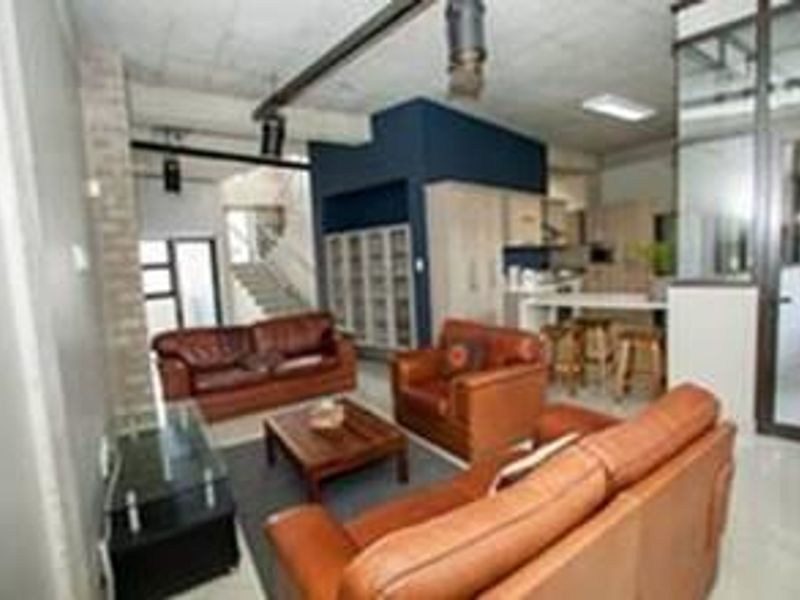 Open-plan living area featuring an industrial-style exposed concrete ceiling, integrated kitchen cabinetry, and a staircase leading to the upper level.