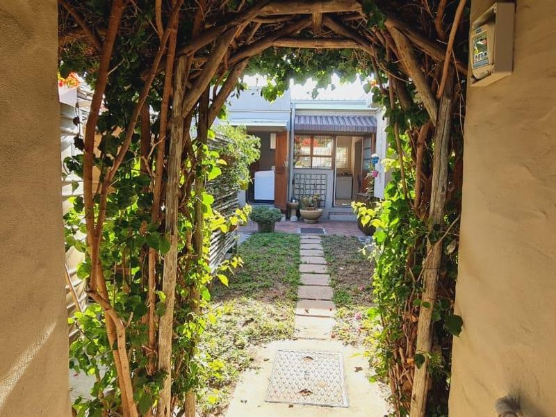 A view through a rustic wooden trellis archway leading into a private rear garden with a stone pathway and established greenery.