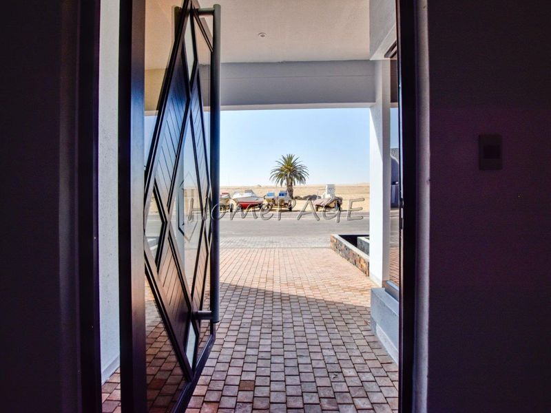 View from the interior looking out through a modern pivot front door onto a paved entryway.