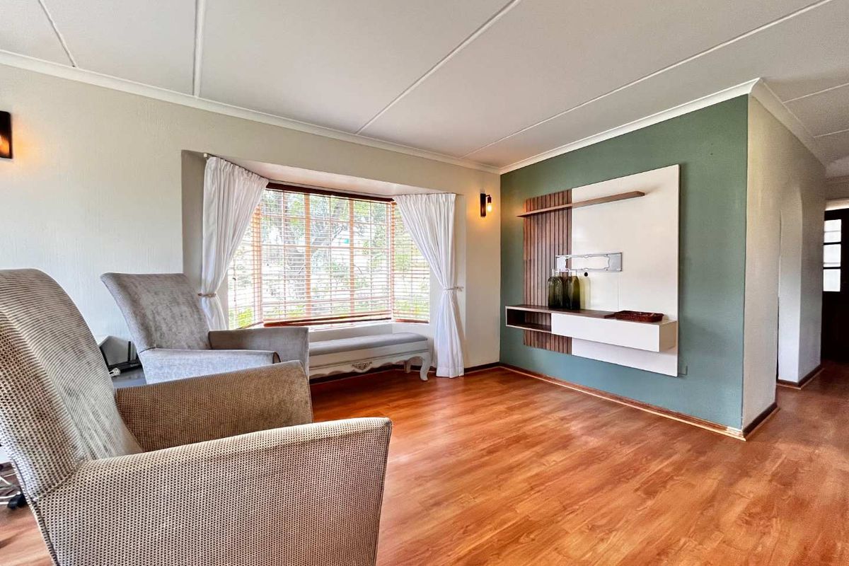 A bright living room featuring warm wood-look flooring, a large bay window, and a modern built-in media wall unit with decorative paneling.