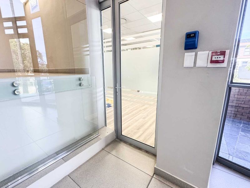 Modern office entrance area featuring glass partitioning, aluminium door frames, and integrated security and fire safety systems with clean tiled flooring.
