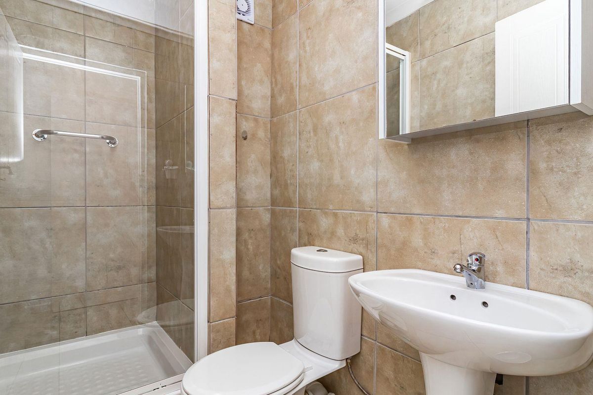 A functional bathroom featuring a glass-enclosed shower, pedestal basin, and wall-mounted medicine cabinet with neutral floor-to-ceiling tiling.